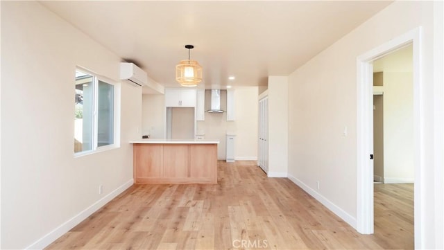 kitchen featuring light wood-style flooring, a peninsula, white cabinetry, an AC wall unit, and wall chimney range hood