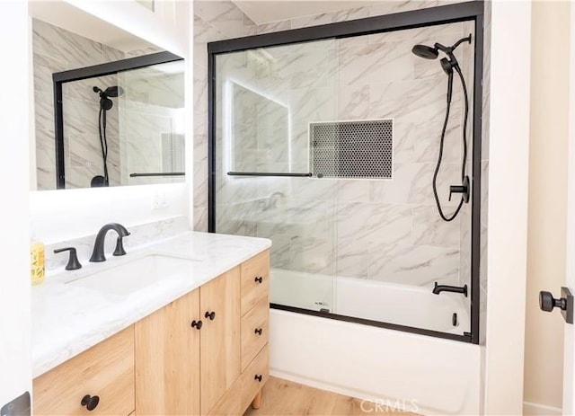 full bath with bath / shower combo with glass door, wood finished floors, and vanity