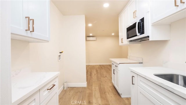 kitchen featuring light wood finished floors, white cabinets, light stone countertops, a sink, and recessed lighting