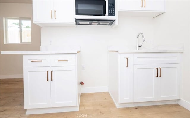 kitchen with white cabinets, light countertops, baseboards, and light wood finished floors