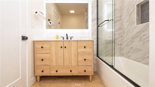 bathroom featuring bath / shower combo with glass door, wood finished floors, and vanity