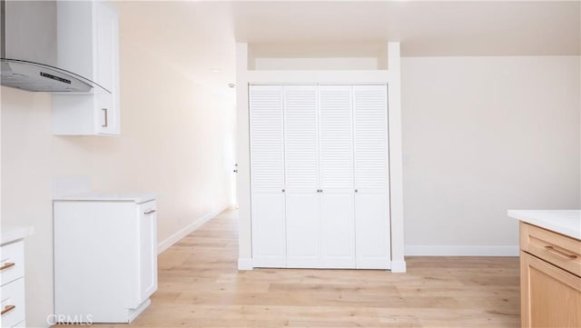 interior space featuring baseboards, wall chimney exhaust hood, light countertops, and light wood-style floors