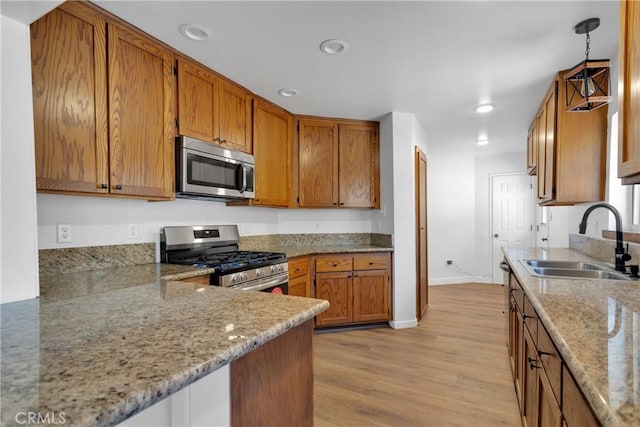 kitchen featuring stainless steel appliances, light wood-type flooring, hanging light fixtures, light stone countertops, and sink