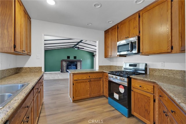 kitchen featuring appliances with stainless steel finishes, light wood-type flooring, kitchen peninsula, a fireplace, and sink