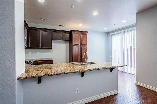 kitchen featuring dark wood-type flooring, sink, light stone counters, kitchen peninsula, and a breakfast bar area