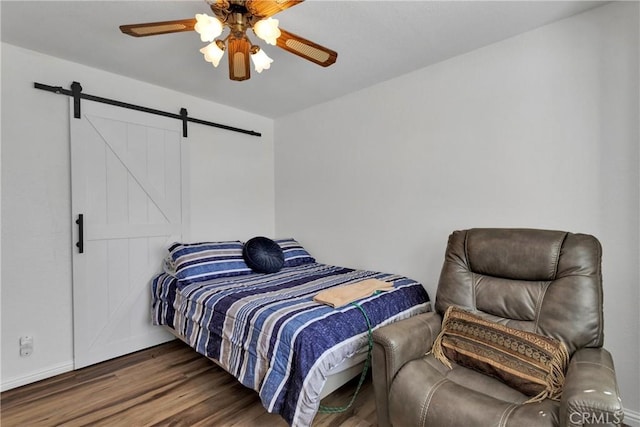 bedroom featuring dark hardwood / wood-style flooring, a barn door, and ceiling fan