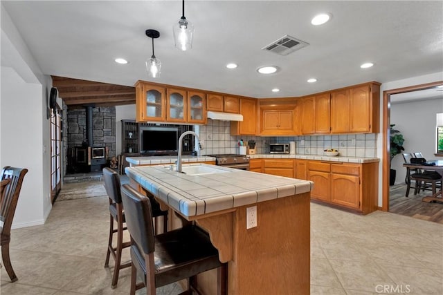 kitchen with decorative backsplash, sink, pendant lighting, a wood stove, and tile counters