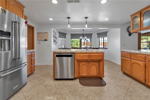 kitchen featuring tile counters, hanging light fixtures, stainless steel appliances, an inviting chandelier, and light tile patterned floors