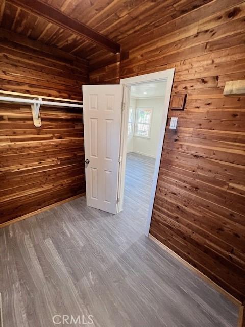 unfurnished bedroom featuring beamed ceiling, wood walls, wooden ceiling, and dark wood-type flooring