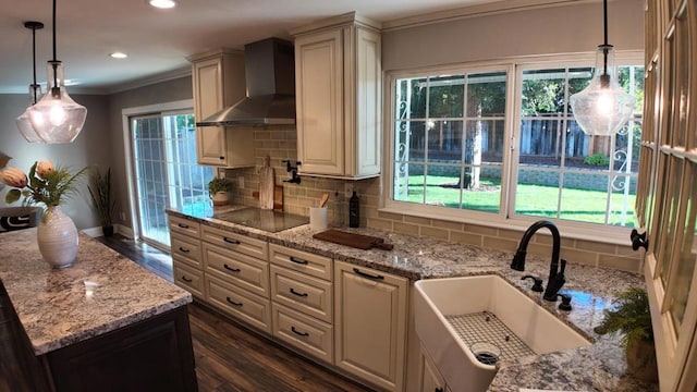 kitchen featuring wall chimney exhaust hood, sink, light stone counters, black electric cooktop, and backsplash