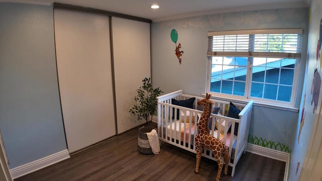 bedroom featuring crown molding, wood-type flooring, a closet, and a crib