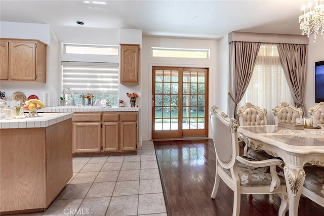 kitchen featuring light brown cabinetry, sink, an inviting chandelier, light hardwood / wood-style flooring, and tile counters