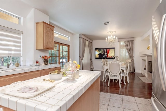 kitchen with a center island, a tile fireplace, stainless steel fridge, tile counters, and light hardwood / wood-style floors