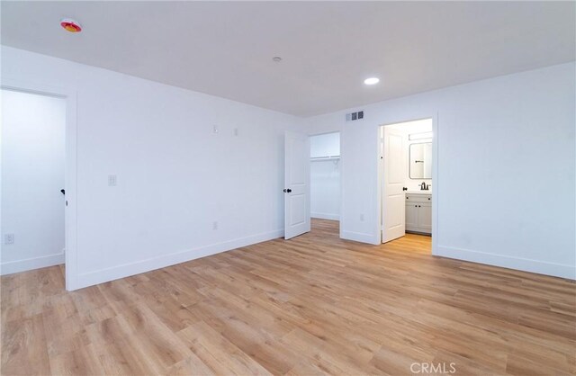 unfurnished bedroom featuring a walk in closet, ensuite bathroom, and light hardwood / wood-style floors