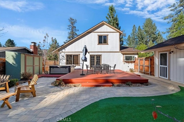 rear view of property featuring a storage shed, a patio, a wooden deck, and a hot tub