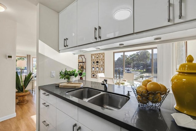 kitchen with sink, white cabinets, light hardwood / wood-style flooring, and dark stone counters