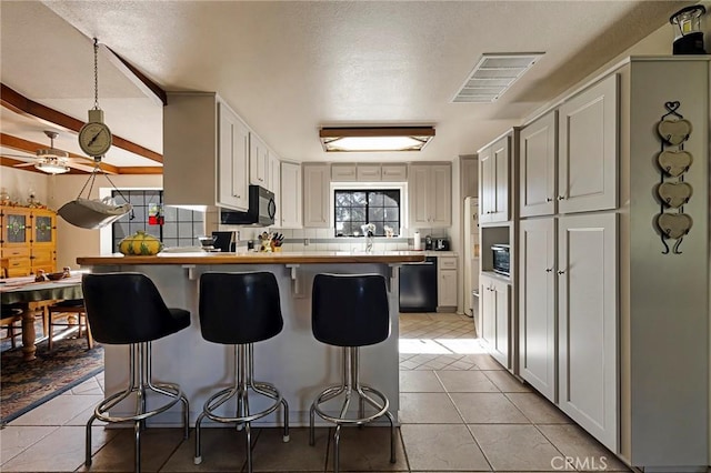 kitchen featuring black appliances, a breakfast bar, light tile patterned flooring, and white cabinets