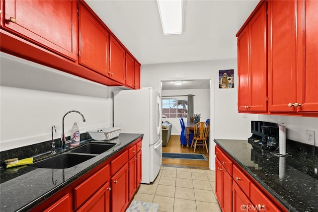 kitchen with light tile patterned flooring, sink, white fridge, and dark stone counters