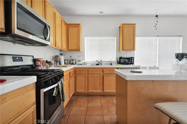 kitchen featuring sink, tile counters, light tile patterned floors, and appliances with stainless steel finishes