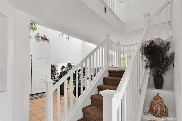 stairs with tile patterned flooring, a healthy amount of sunlight, and a towering ceiling