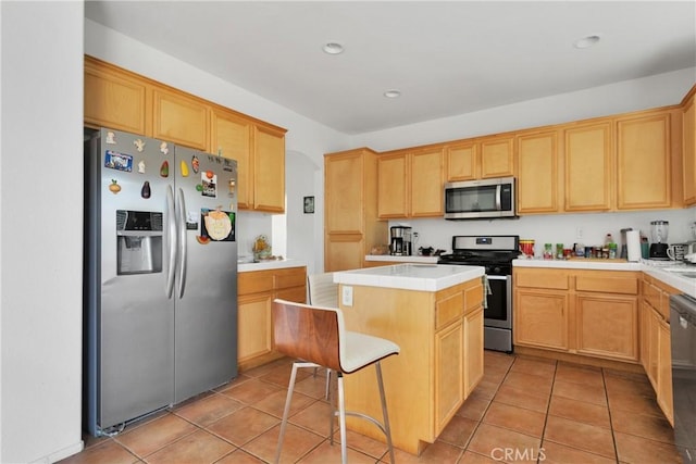 kitchen with a kitchen bar, stainless steel appliances, light brown cabinets, a center island, and light tile patterned flooring