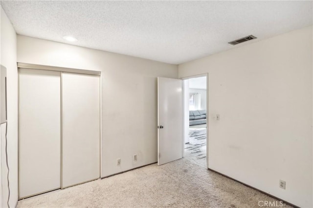 unfurnished bedroom featuring light colored carpet, a textured ceiling, and a closet