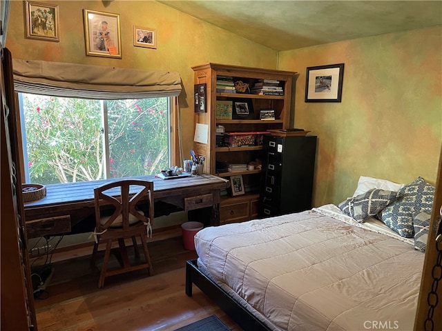 bedroom featuring wood-type flooring, vaulted ceiling, and a textured wall