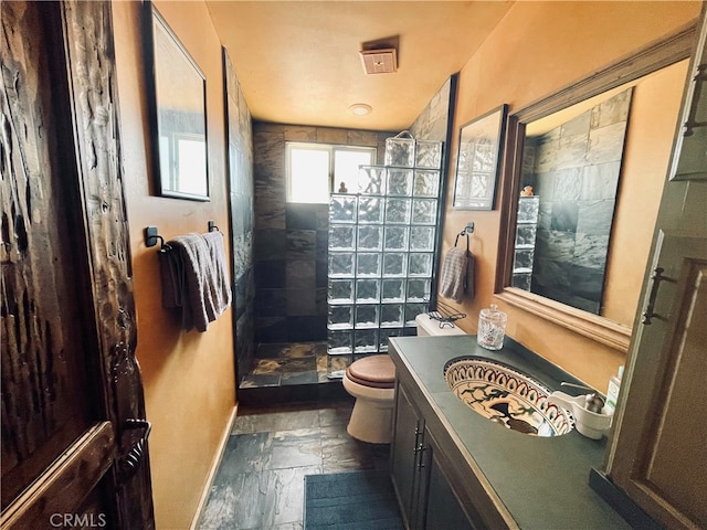 bathroom with tiled shower, vanity, and toilet