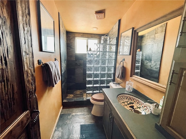 full bathroom featuring toilet, stone tile floors, vanity, and a walk in shower