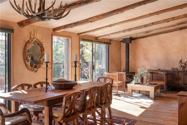 dining area with hardwood / wood-style floors, a wood stove, and beamed ceiling