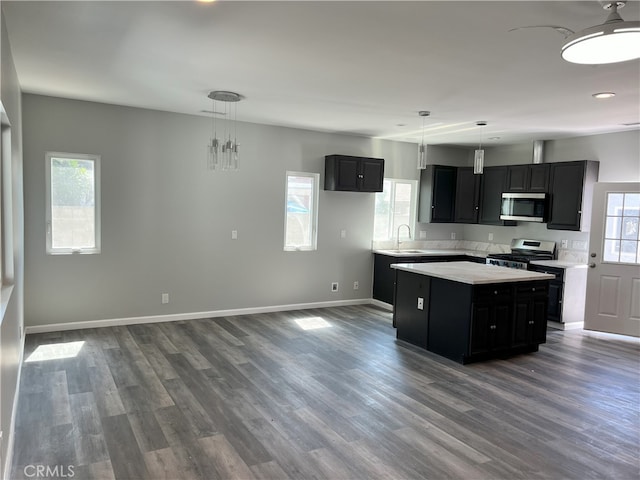 kitchen with dark wood-type flooring, sink, hanging light fixtures, appliances with stainless steel finishes, and a kitchen island