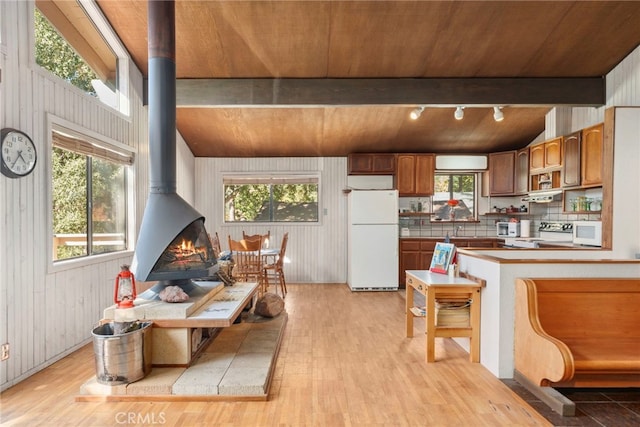 kitchen with light hardwood / wood-style floors, wood walls, white appliances, and a wood stove