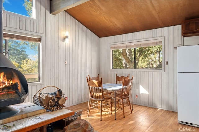 dining area featuring wooden walls, a wood stove, wood ceiling, and light hardwood / wood-style flooring