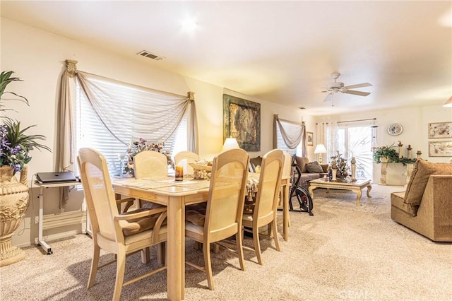 dining space with ceiling fan and light colored carpet