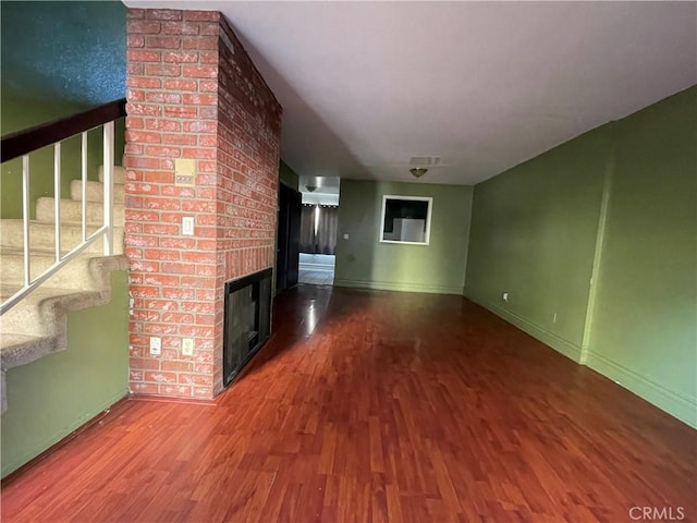 unfurnished living room with wood-type flooring and a brick fireplace