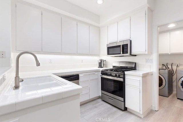 kitchen with washing machine and clothes dryer, tile counters, white cabinets, and stainless steel appliances