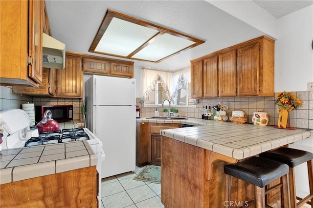 kitchen with tile counters, a kitchen breakfast bar, kitchen peninsula, white fridge, and decorative backsplash