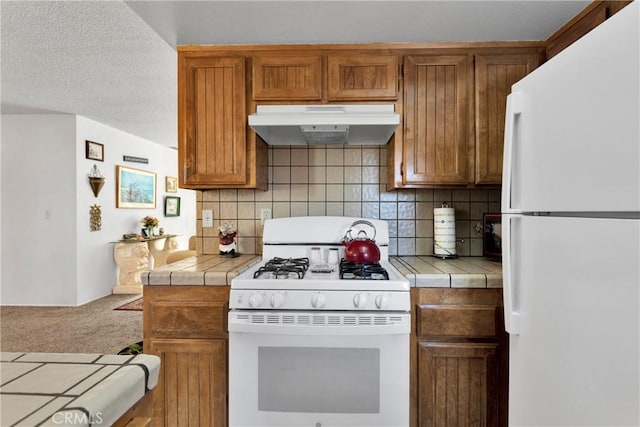 kitchen featuring a textured ceiling, decorative backsplash, tile counters, and white appliances