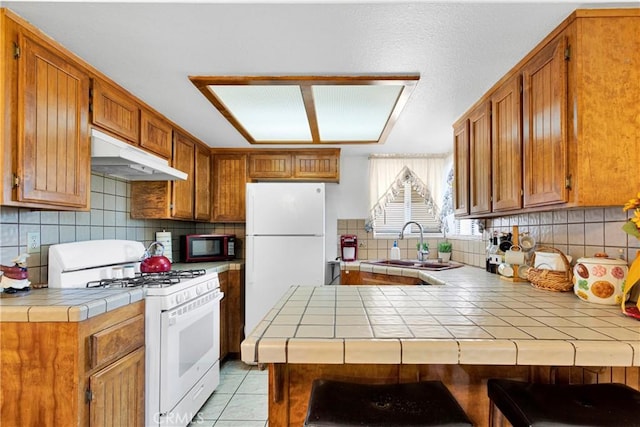 kitchen featuring kitchen peninsula, decorative backsplash, white appliances, sink, and tile counters