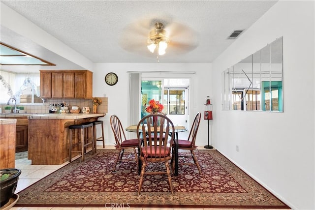 dining area with ceiling fan, sink, light tile patterned flooring, and a textured ceiling