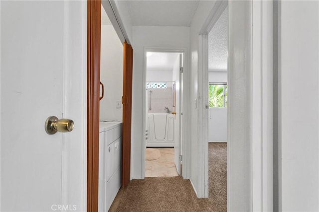 hallway featuring washer / clothes dryer, light carpet, and a textured ceiling