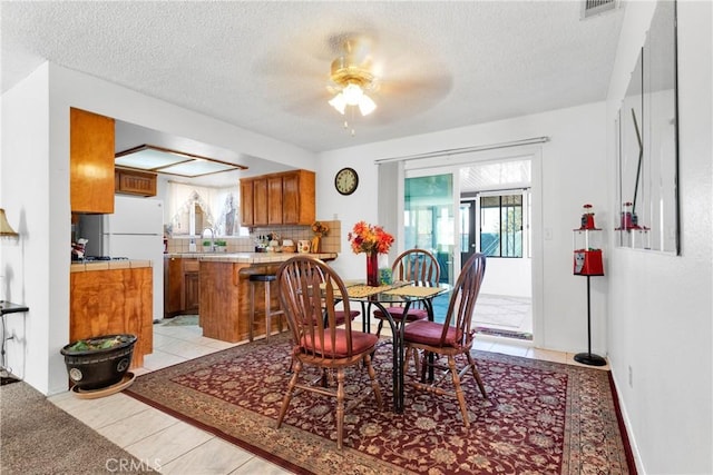 dining space with ceiling fan, sink, light tile patterned floors, and a textured ceiling