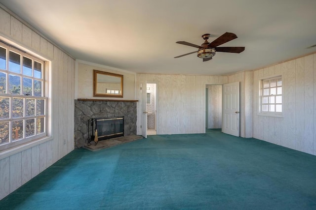 unfurnished living room featuring carpet floors, ceiling fan, wood walls, and a stone fireplace