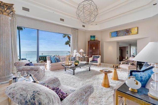 living room with a raised ceiling, a water view, and a notable chandelier