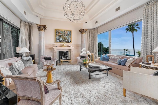 living room featuring a tray ceiling, a water view, and an inviting chandelier