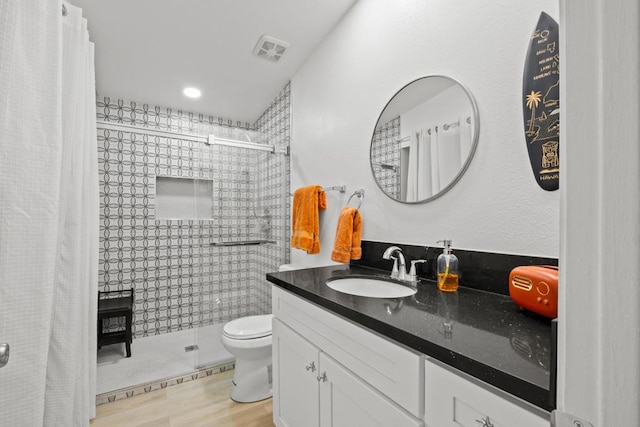 bathroom featuring toilet, tiled shower, wood-type flooring, and vanity