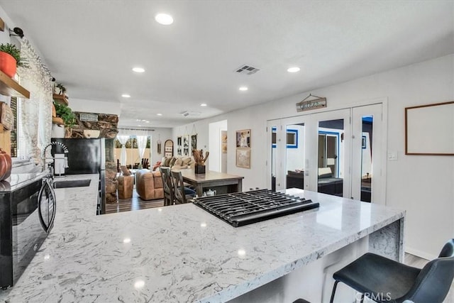 kitchen with a breakfast bar, french doors, sink, light stone counters, and kitchen peninsula