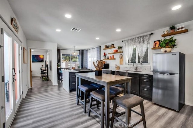 kitchen with decorative light fixtures, stainless steel fridge, sink, and light hardwood / wood-style flooring