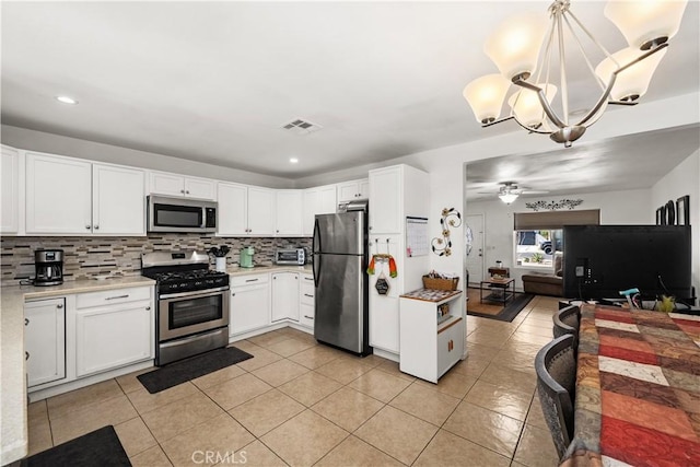 kitchen featuring ceiling fan with notable chandelier, pendant lighting, white cabinets, decorative backsplash, and stainless steel appliances