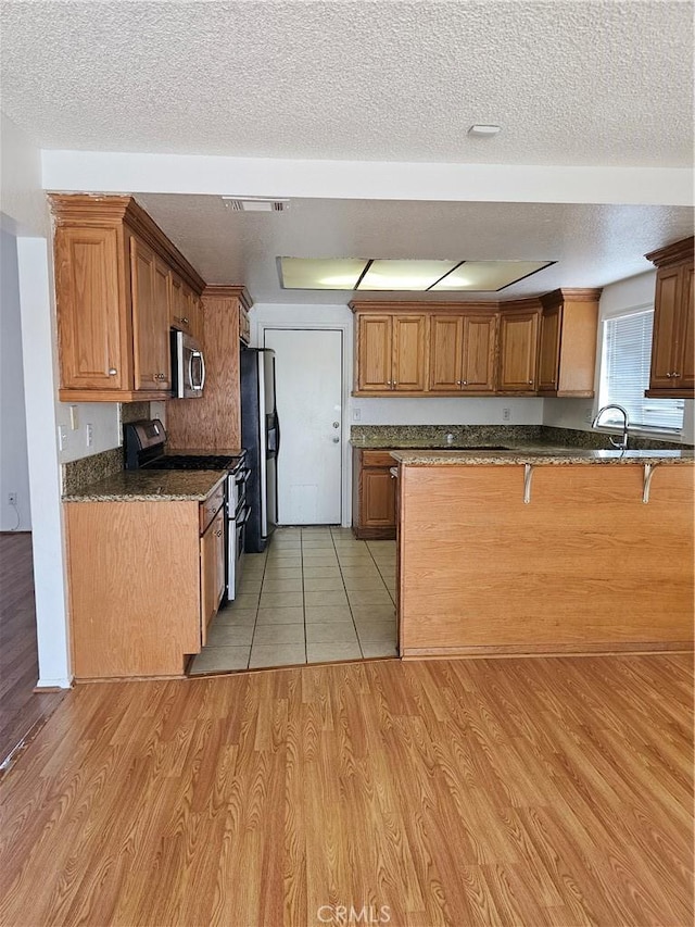 kitchen featuring dark stone counters, light hardwood / wood-style flooring, a textured ceiling, appliances with stainless steel finishes, and kitchen peninsula